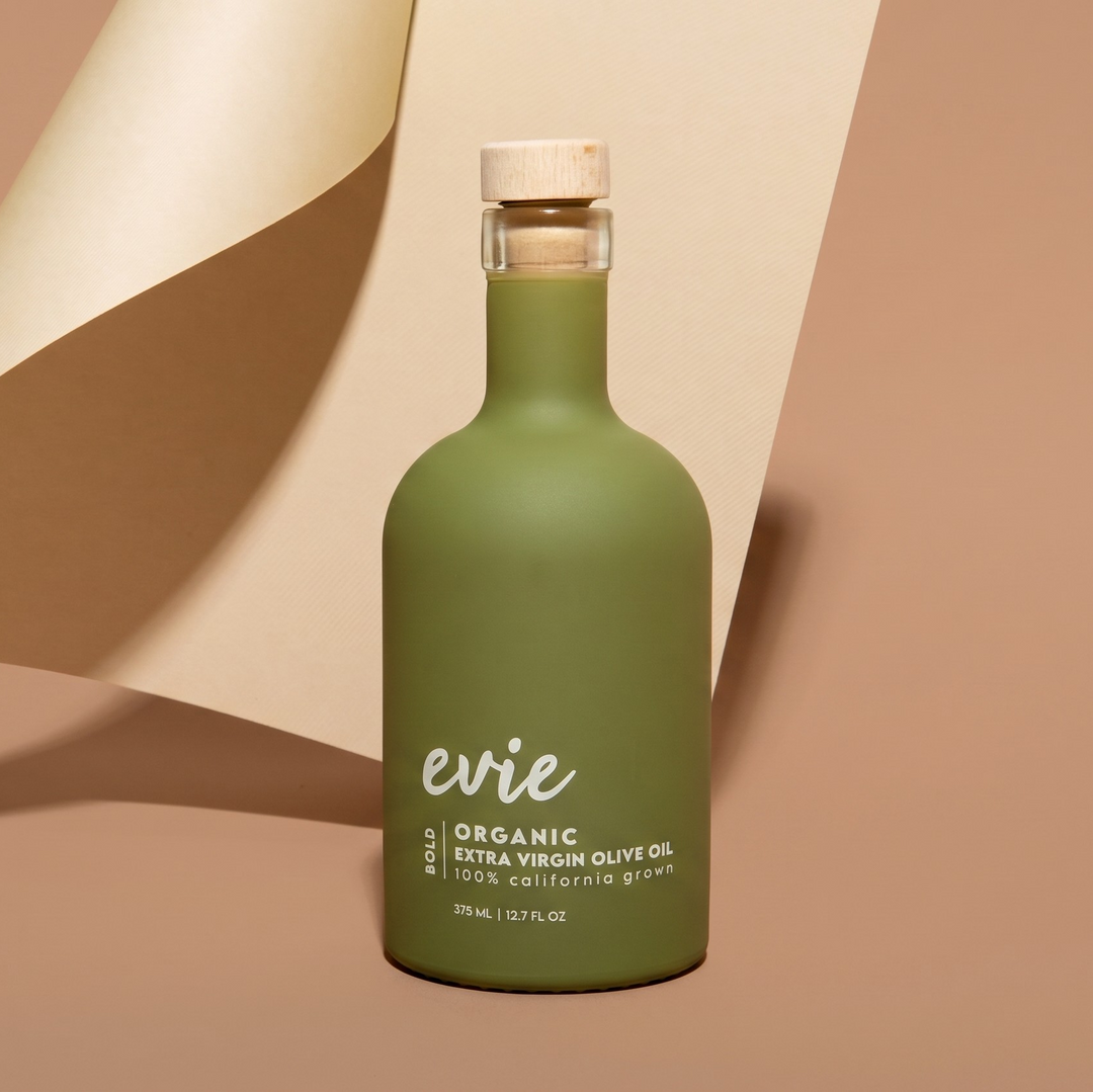 Green bottle of evie organic extra virgin olive oil on a beige background