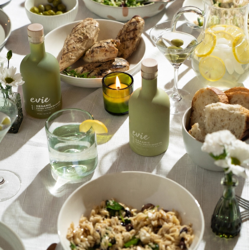 Table setting with bowls of food, bread, and bottles on a white tablecloth.